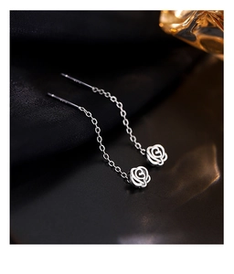 Macro shot of S925 sterling silver rose drop earrings with delicate chain on silk background