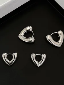 Macro shot of two pairs of heart-shaped S925 sterling silver hoop earrings on black stand