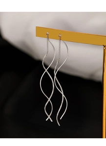 Macro shot of long silver wavy spiral earrings on a gold stand with blurred background
