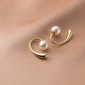 Elegant gold drop earrings with lustrous round white pearls on champagne satin background