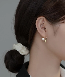 Close-up of elegant gold hook earring with white round pearl on female model