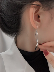 Macro shot of silver minimalist double-twist spiral tassel earrings on model