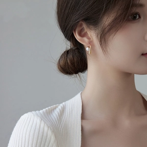Elegant gold teardrop pearl earrings worn by a model in a minimalist style