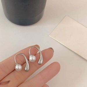 Detail of silver U-shaped pearl earrings featuring water drop pendants held by hand
