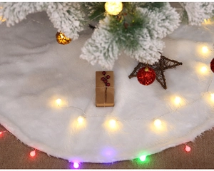 Close-up of white faux fur Christmas tree skirt with warm LED lights and holiday decor