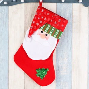Large red Christmas stocking with Santa Claus and sequin tree on striped wood background