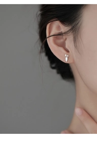 Close-up of small silver rabbit and carrot earring worn by a model on a grey background