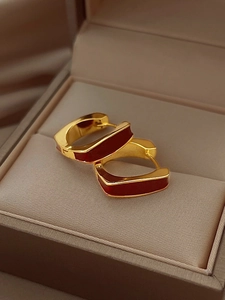 Detailed close-up of gold geometric earrings with dark red enamel in a jewelry box