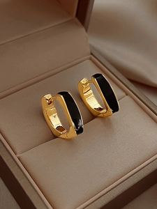 Detail of square gold hoop earrings with black enamel inlay on beige silk texture
