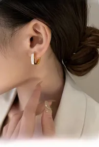 Close-up of elegant gold U-shaped enamel hoop earrings worn by a model in a white suit