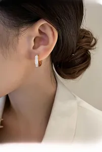 Close-up of elegant gold square hoop earring with white enamel inlay worn by model