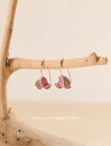 Macro shot of pink tulip earrings with silver hooks hanging on a natural wooden branch