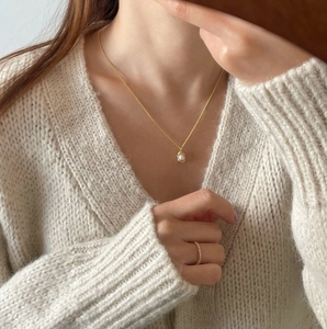 Elegant gold pearl peanut necklace and slim diamond ring on model in beige knit sweater
