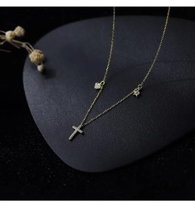 Detail of gold-tone necklace with zircon heart, star, and cross charms on dark backdrop