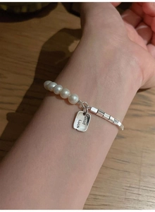 Detail of S925 silver bracelet with pearls and Good Luck engraved rectangular pendant