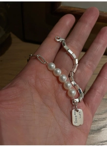 Close-up of S925 sterling silver Luck tag and pearl chain detail on the bracelet