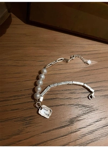 Macro shot of S925 silver bracelet featuring white pearls and Good Luck letter tag