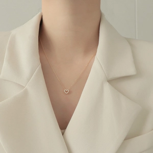 Nahaufnahme einer goldenen hohlen Herz-Halskette mit Kristallen auf einem weißen Blazer