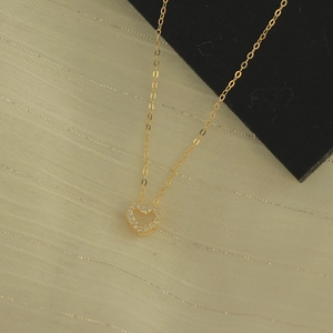 Goldene S925 Silberkette mit hohlem Herzanhänger und Zirkonia auf gestreiftem Stoff