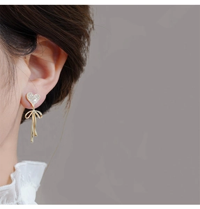Close-up of S925 silver heart stud earrings with zircon inlay and golden bow drop detail