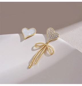 Close-up of asymmetric S925 silver heart earrings with pearl shells and gold ribbons