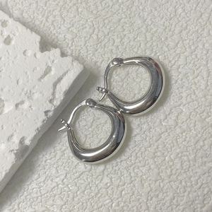 Créoles en argent poli sur pierre blanche avec un fond texturé au style minimaliste