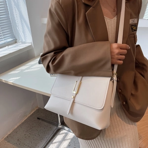 Close-up of white crossbody bag with gold metal buckle on a brown blazer outfit