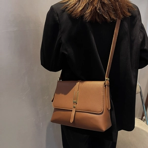 Detail of a brown leather shoulder bag with vertical strap and gold metal buckle