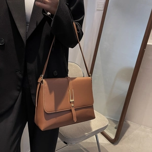 Close-up of brown leather flap shoulder bag with gold buckle on black blazer