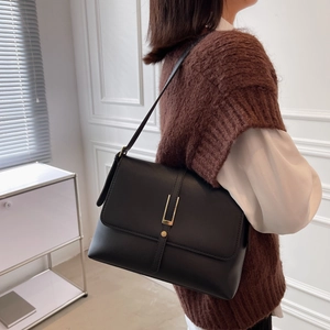 Detail of elegant black faux leather shoulder bag with golden buckle and contrast stitching