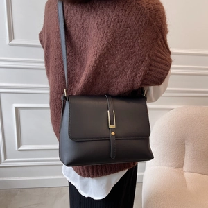 Detailed view of a black leather crossbody bag with golden buckle on a stylish model