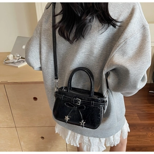 Détail d'un sac à main noir brillant avec nœud papillon et breloques étoiles sur la bandoulière