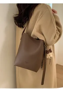 Close-up of brown pebbled leather bucket bag with teddy bear charm and gold logo detail