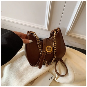 Detailed view of dark brown crescent chain bag with golden hardware on a textured surface