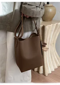 Detailed view of dark brown bucket bag with lychee grain texture and plush bear charm