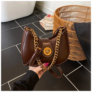 Detail of a dark brown half-moon bag featuring a thick gold chain and a twist lock clasp