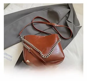 Detail showing brown glossy leather shoulder bag with chic metal chain and strap