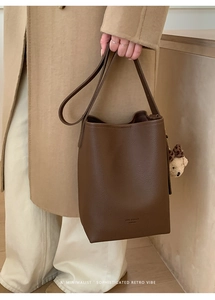 Detail of dark brown pebble leather bucket bag featuring a decorative bear charm