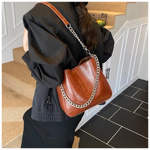 Close-up of caramel brown bucket bag with shiny PU leather and thick metal chain detail