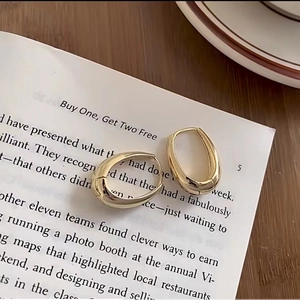 Minimalist gold oval geometric hoop earrings displayed on a vintage book page