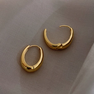 Detail of chunky gold oval hoop earrings with a high-polish mirror finish on fabric