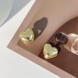 Polished gold heart hoop earrings with creative shadow on a minimalist background