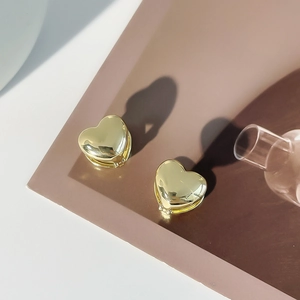 Macro shot of polished gold heart-shaped metal earrings with a hinged closure detail