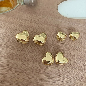 Close-up of three pairs of 3D polished gold heart earrings on a natural wood surface