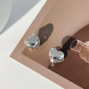 Detailed view of 3D heart-shaped polished metal stud earrings with soft artistic shadows
