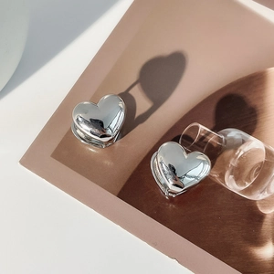 Polished silver heart-shaped stud earrings casting a heart shadow on textured background