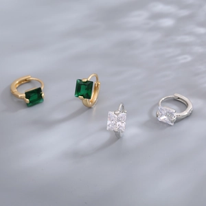 Macro detail of square-cut emerald and clear zircon hoop earrings in gold and silver