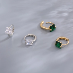 Macro view of emerald and square zircon huggie hoop earrings with four-prong settings