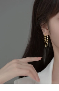 Detail of layered gold lip chain tassel earrings worn by a model in minimalist style