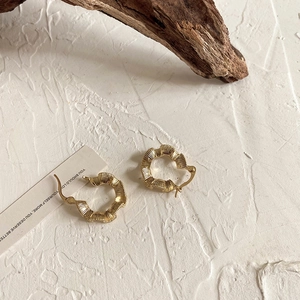 Macro detail of gold wavy ruffle hoop earrings with vintage radial texture on white background